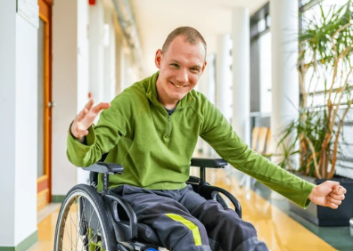 A smiling man in a green shirt using a wheelchair
